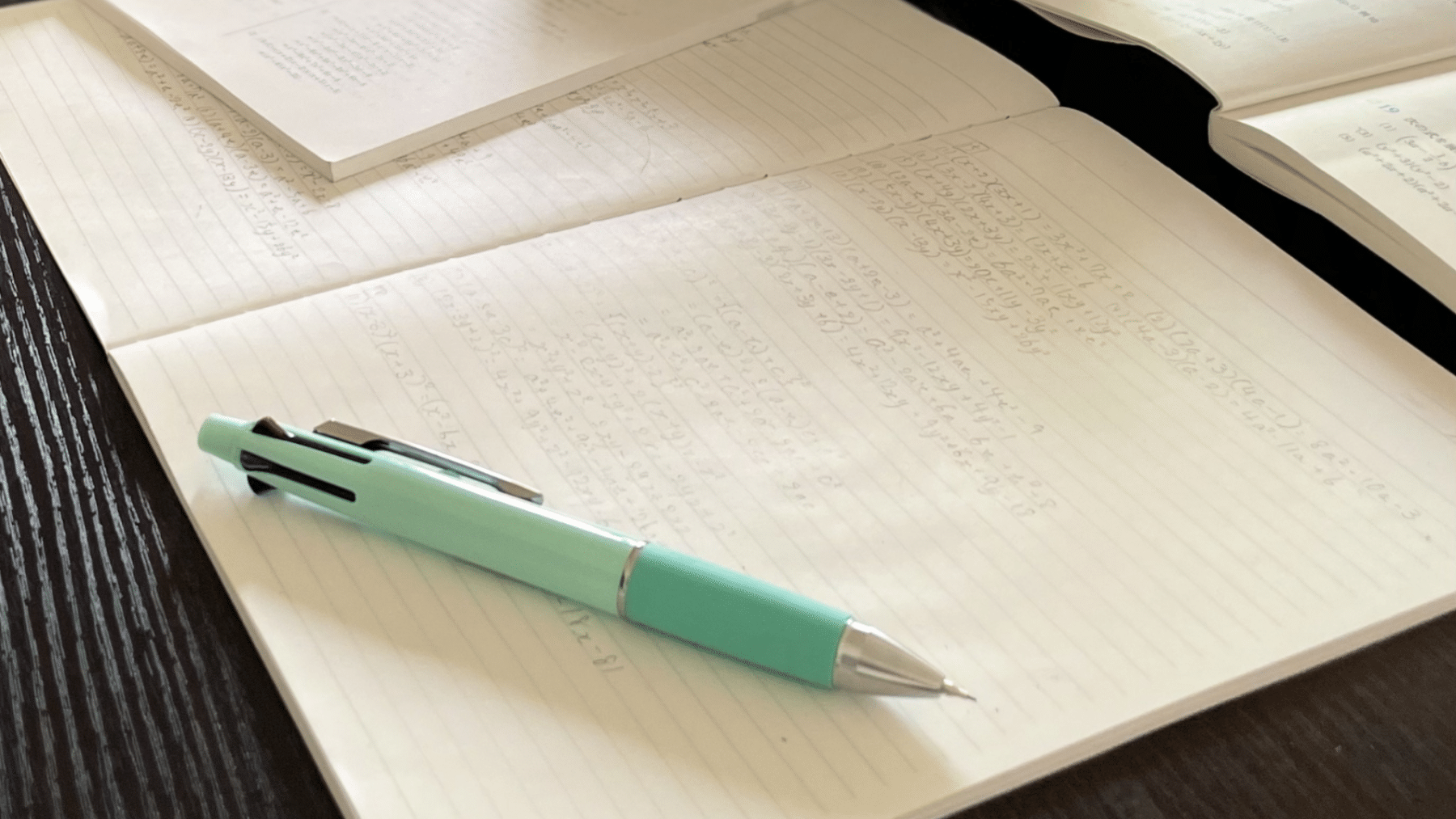 A pen resting on an open notebook with algebra problems being worked out.