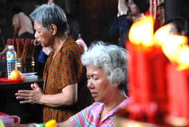 Older women pray by candles at Long-shan temple Buddhismus