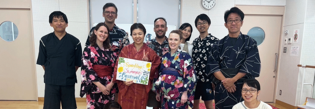 Members of church in traditional summer yukata posing with Summer Festival sign.